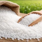 Urea Market Update April; Urea fertilizer granules in a burlap sack with wooden scoop on a farm field background