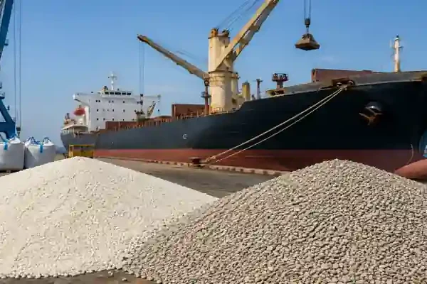 Bulk fertilizer cargo ship unloading DAP and TSP fertilizers at a commercial port, with large fertilizer stockpiles and cranes handling imports from Morocco to India.